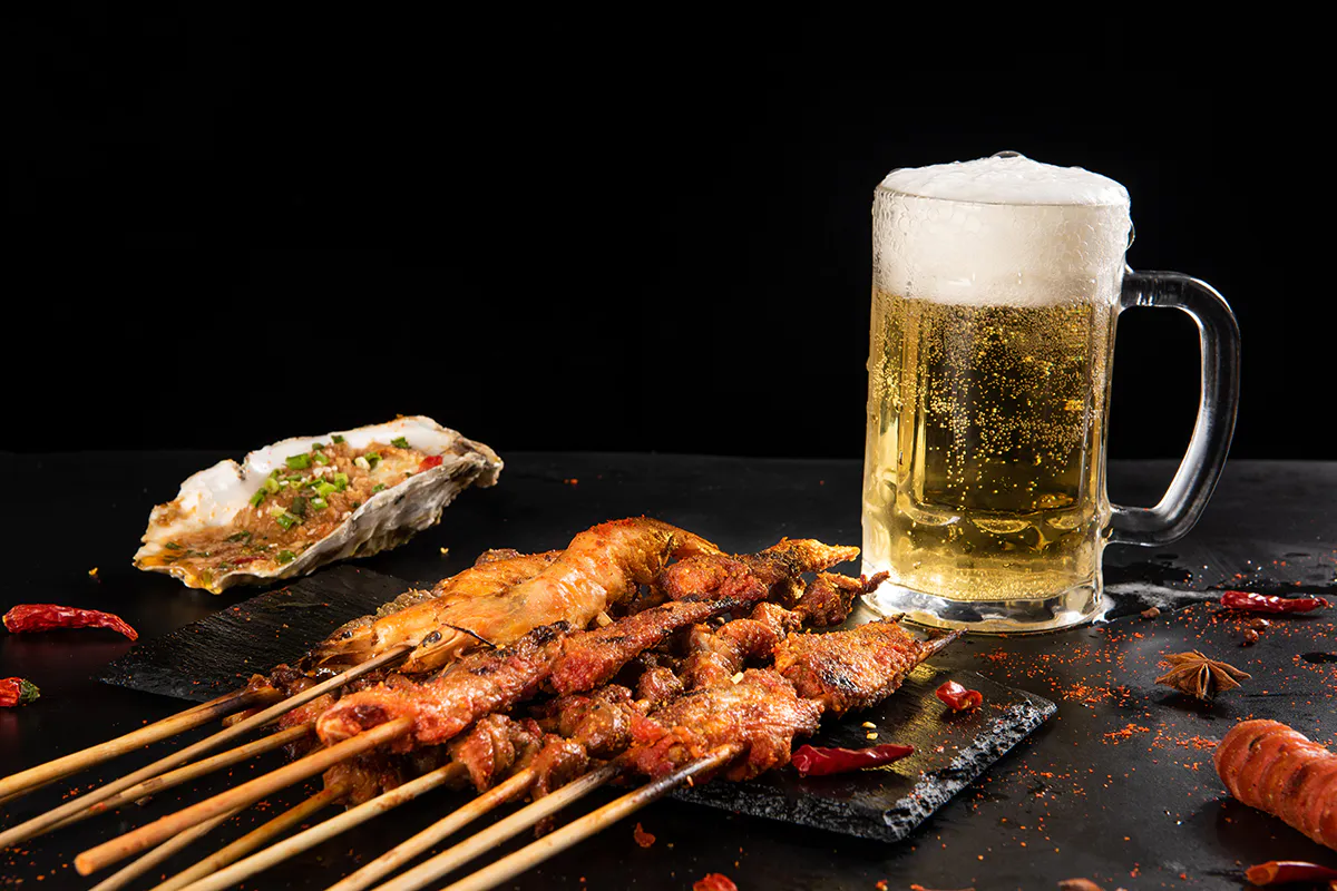 Assorted barbecue skewers with oysters and cold beer at Aquaman BBQ, a Barbecue Restaurant in Queens
